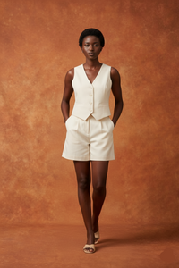 Woman wearing a beige vest and shorts set against a brown background