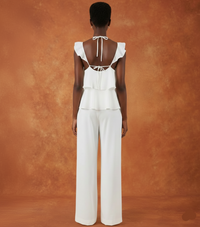 Person wearing a white outfit with ruffled sleeves and wide-leg pants against an orange background